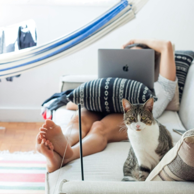 Woman lying on sofa working remotely on laptop